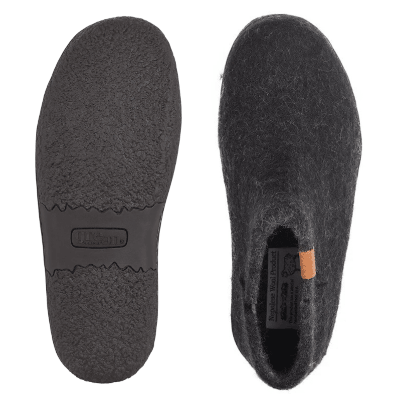 Dois chinelos Green Comfort pretos de feltro de lã, um mostrando a sola de borracha antiderrapante, o outro a parte superior
